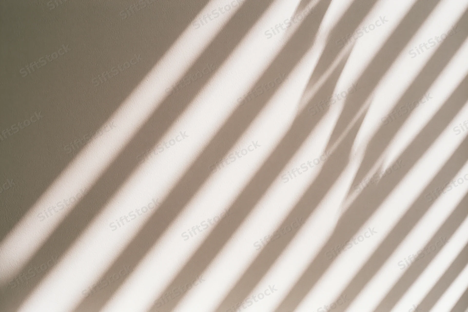 Diagonal shadows from window blinds cast across a plain beige wall