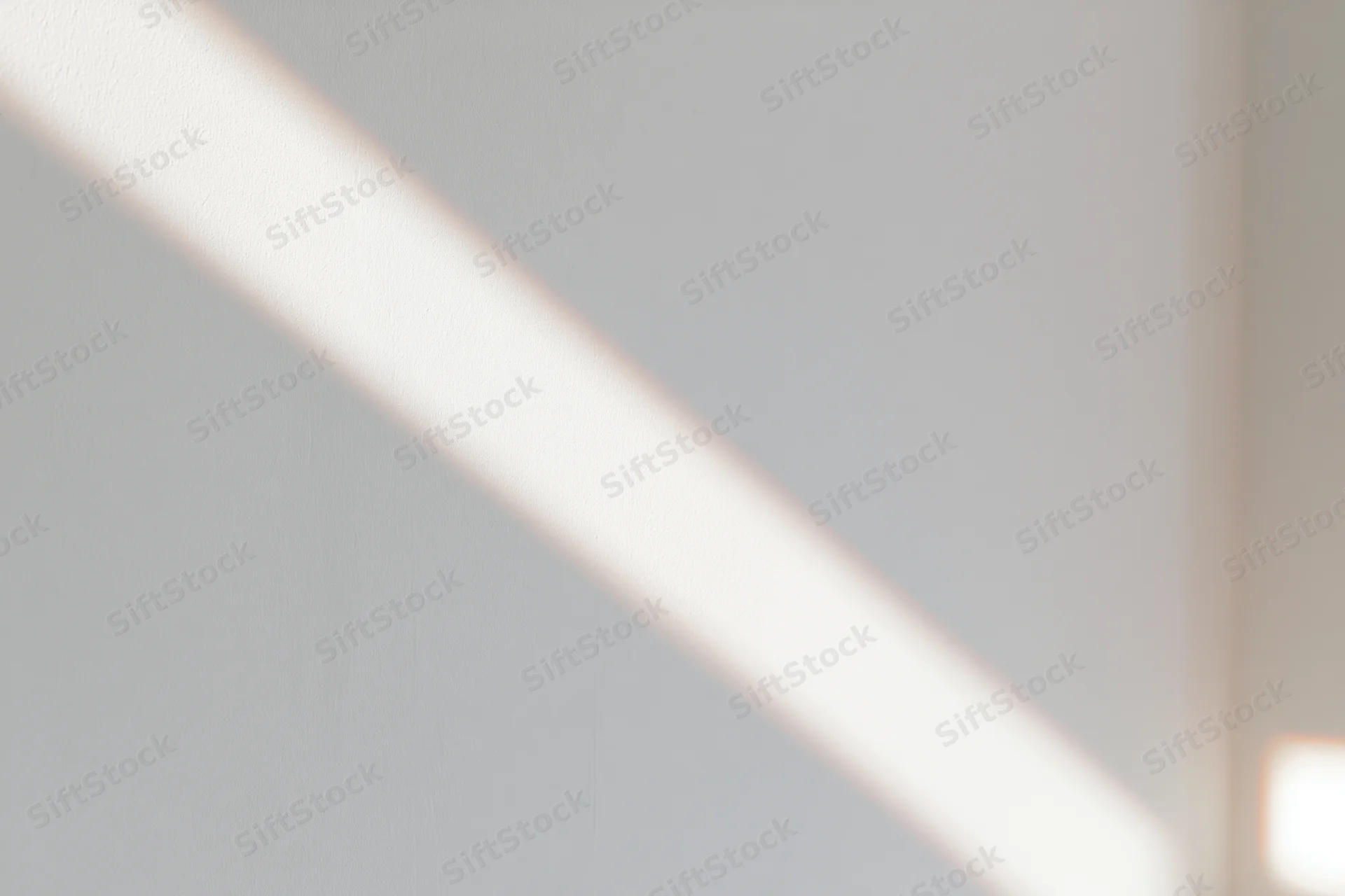 Diagonal strip of natural window light falling across a plain white indoor surface