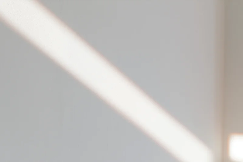 Diagonal strip of natural window light falling across a plain white indoor surface