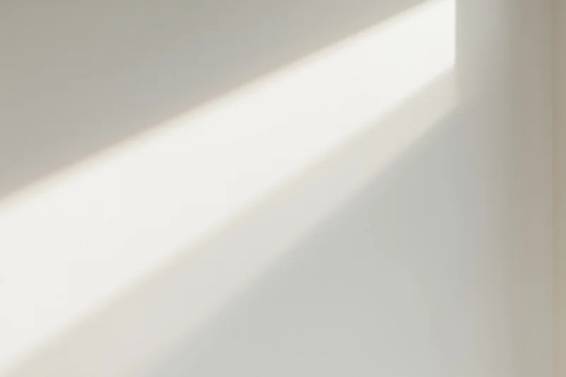 Diagonal strip of natural window light falling across a plain white wall