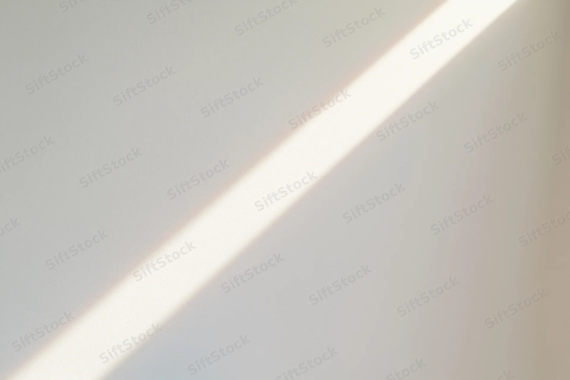Diagonal beam of natural sunlight across a plain white indoor surface