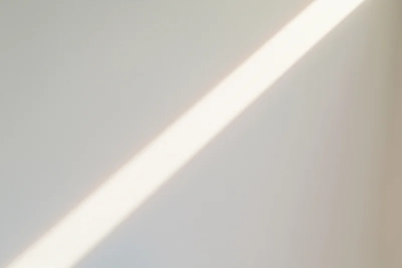 Diagonal beam of natural sunlight across a plain white indoor surface