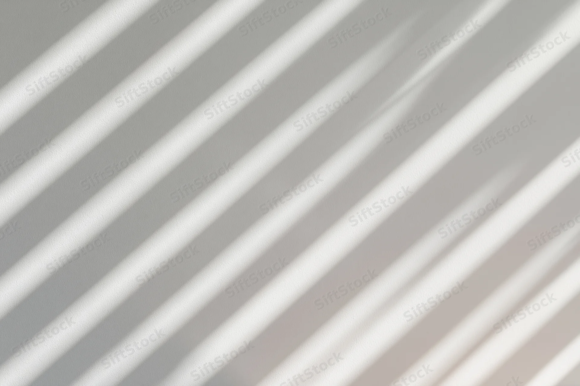 Diagonal shadow stripes from window blinds cast across a white surface