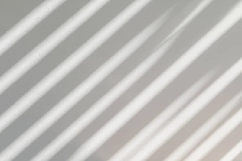 Diagonal shadow stripes from window blinds cast across a white surface