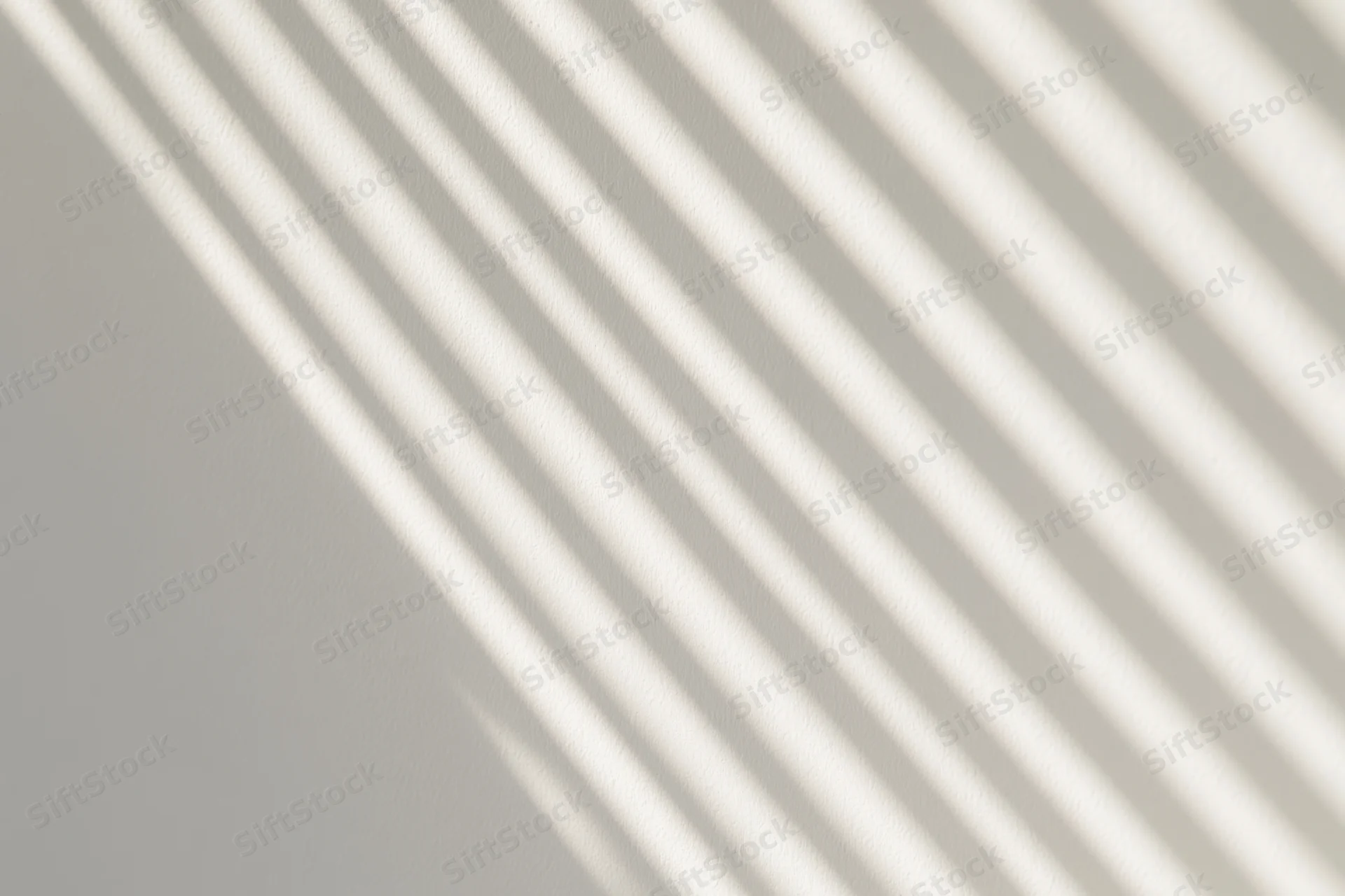 Diagonal shadow stripes from window blinds on a white wall