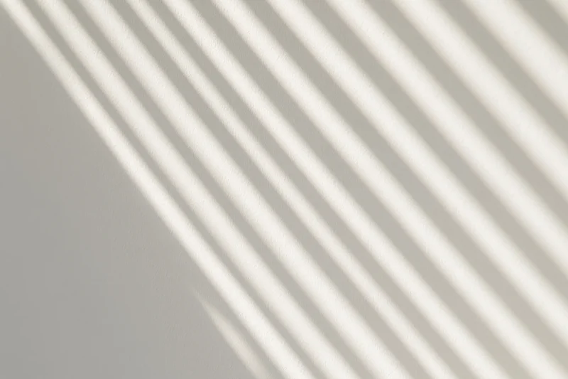 Diagonal shadow stripes from window blinds on a white wall