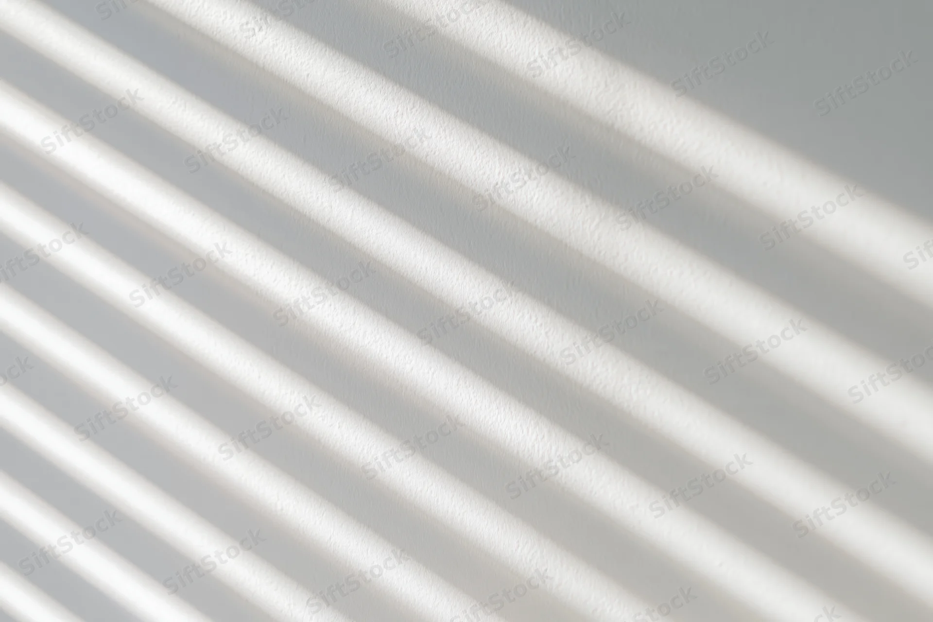 Diagonal light and shadow stripes from window blinds on a white wall