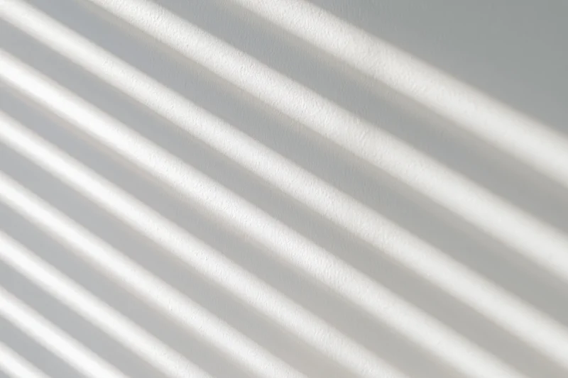 Diagonal light and shadow stripes from window blinds on a white wall