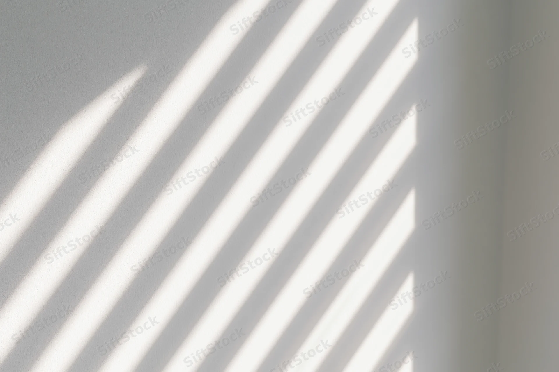 Diagonal light stripes from window blinds cast across a white interior wall