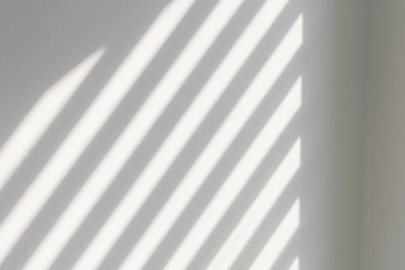 Diagonal light stripes from window blinds cast across a white interior wall