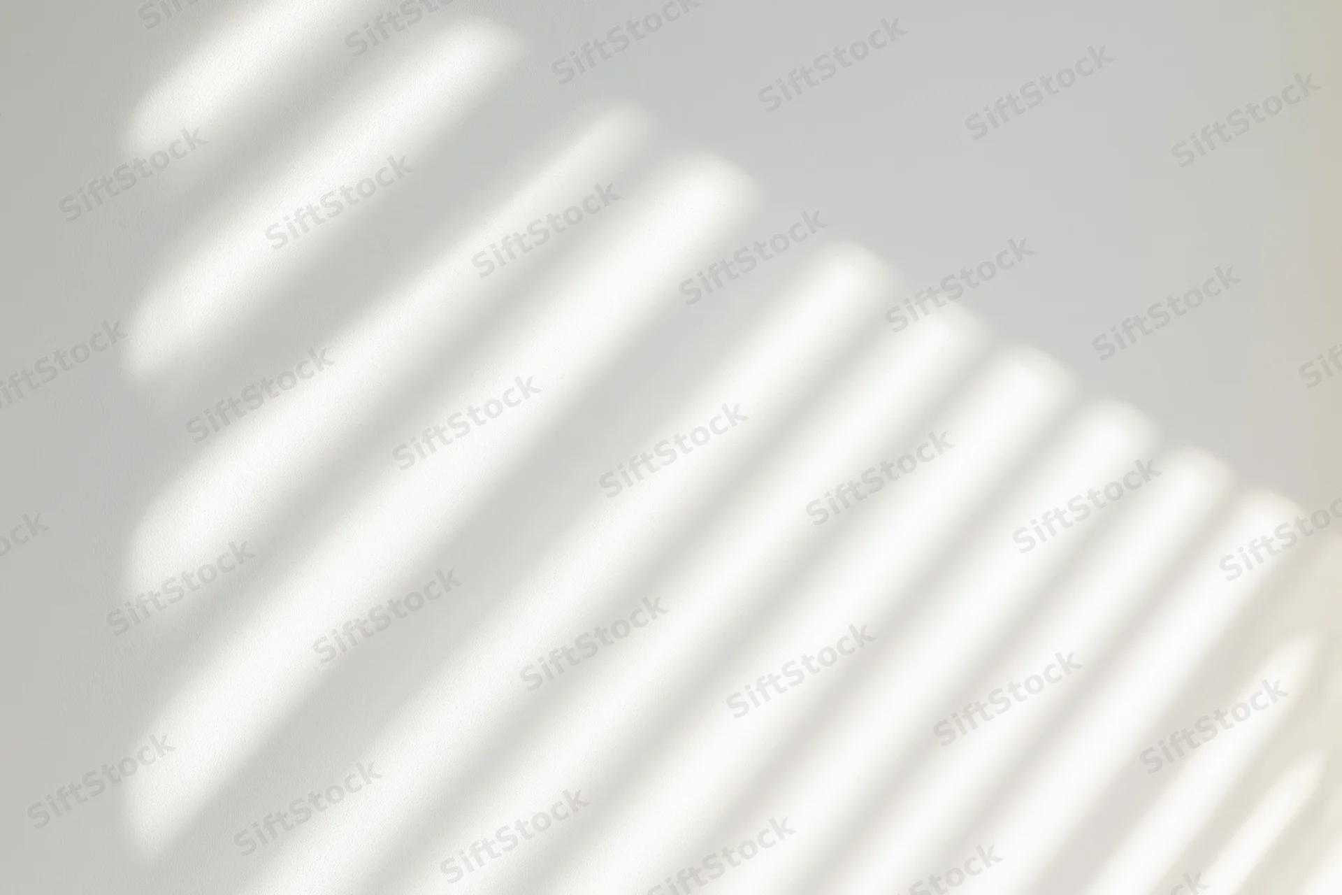 Diagonal shadow stripes from window blinds on a plain white wall