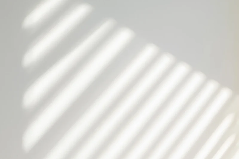Diagonal shadow stripes from window blinds on a plain white wall
