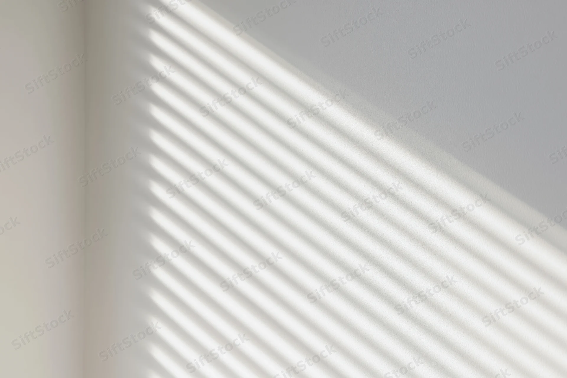 Diagonal shadow stripes from window blinds on a white interior wall