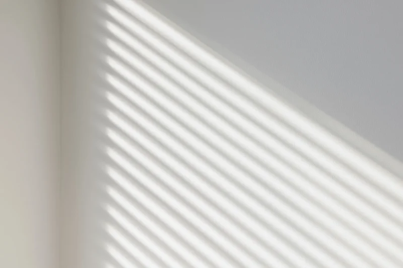 Diagonal shadow stripes from window blinds on a white interior wall