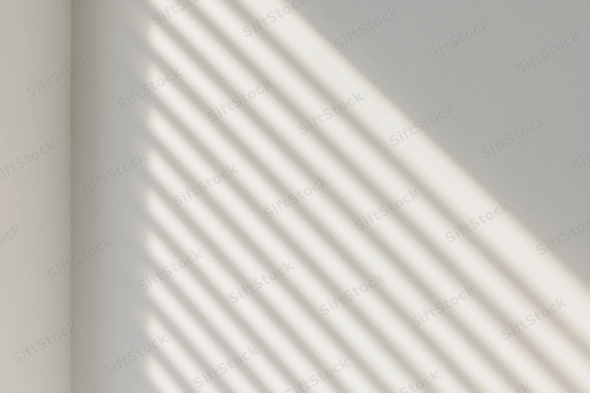Diagonal shadow stripes from window blinds cast across a plain white interior wall