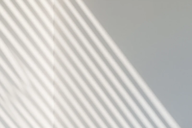 Diagonal shadow stripes from window blinds on a plain wall