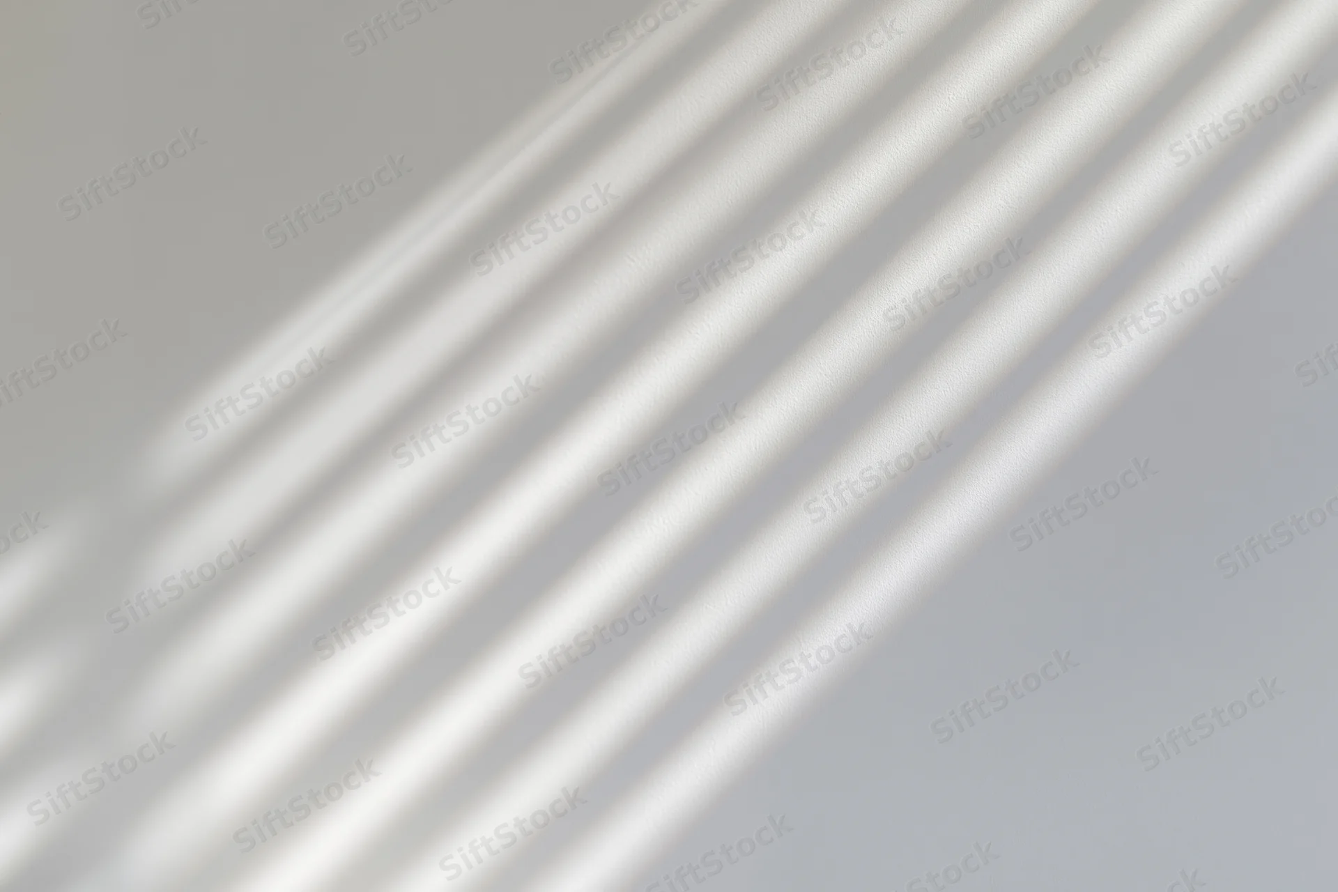 Diagonal light and shadow stripes from window blinds on a plain wall