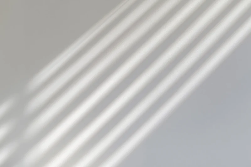 Diagonal light and shadow stripes from window blinds on a plain wall