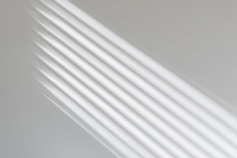 Diagonal light streaks from window blinds on a plain wall
