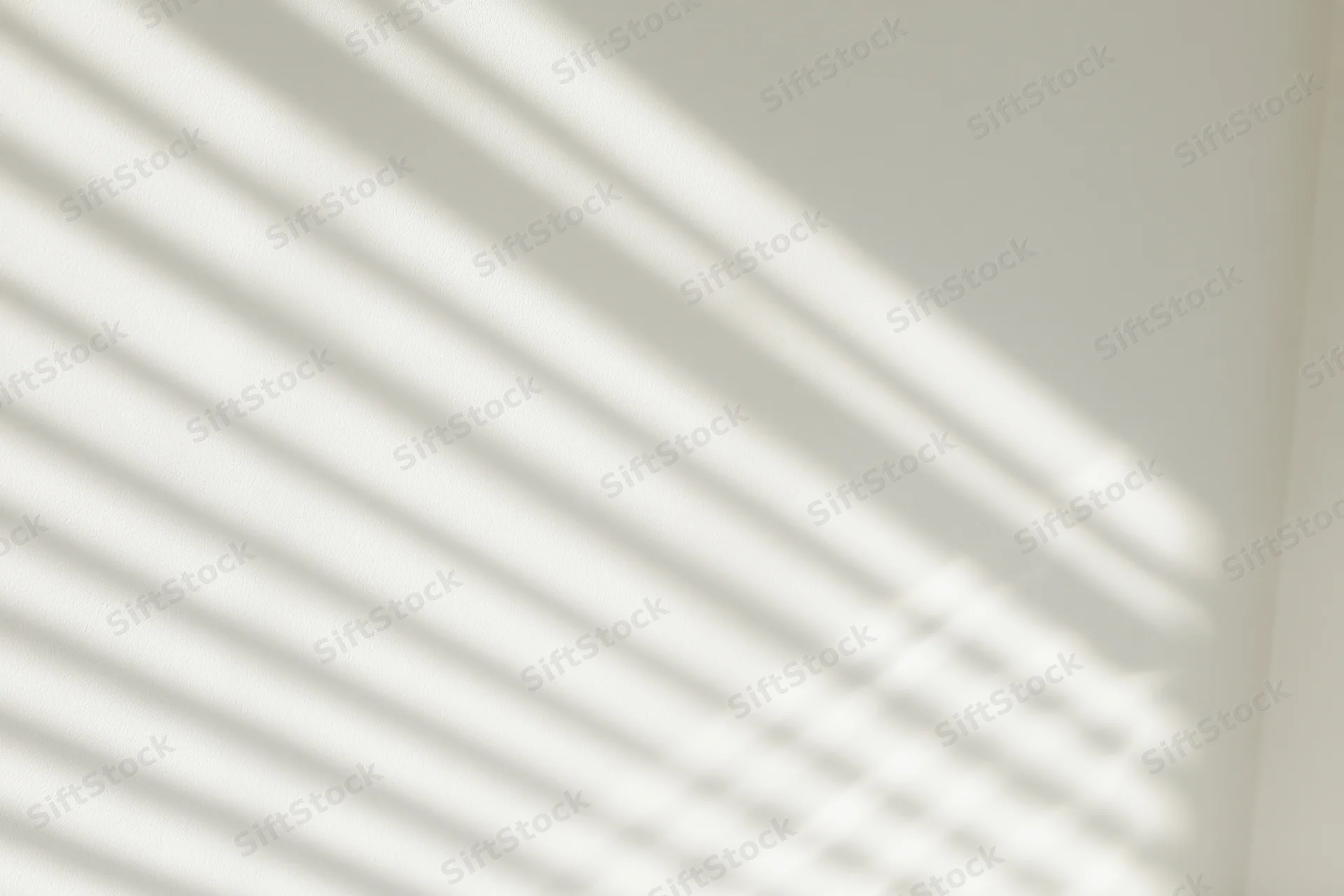 Diagonal light and shadow stripes from window blinds on a white wall