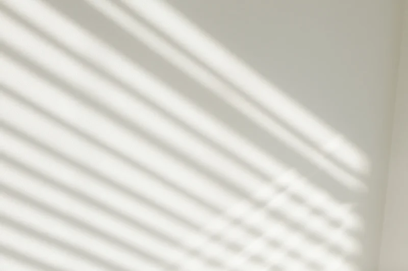 Diagonal light and shadow stripes from window blinds on a white wall