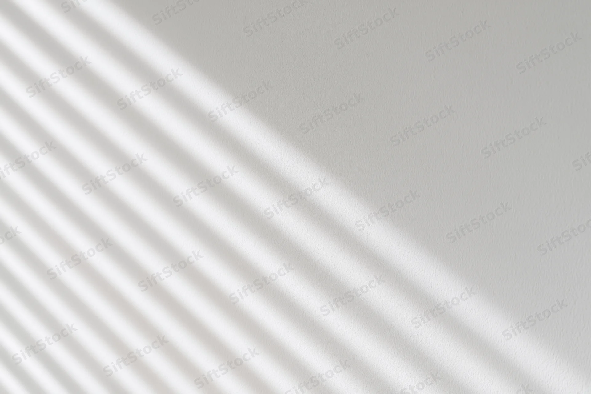 Diagonal shadows from window blinds cast across a plain white interior wall