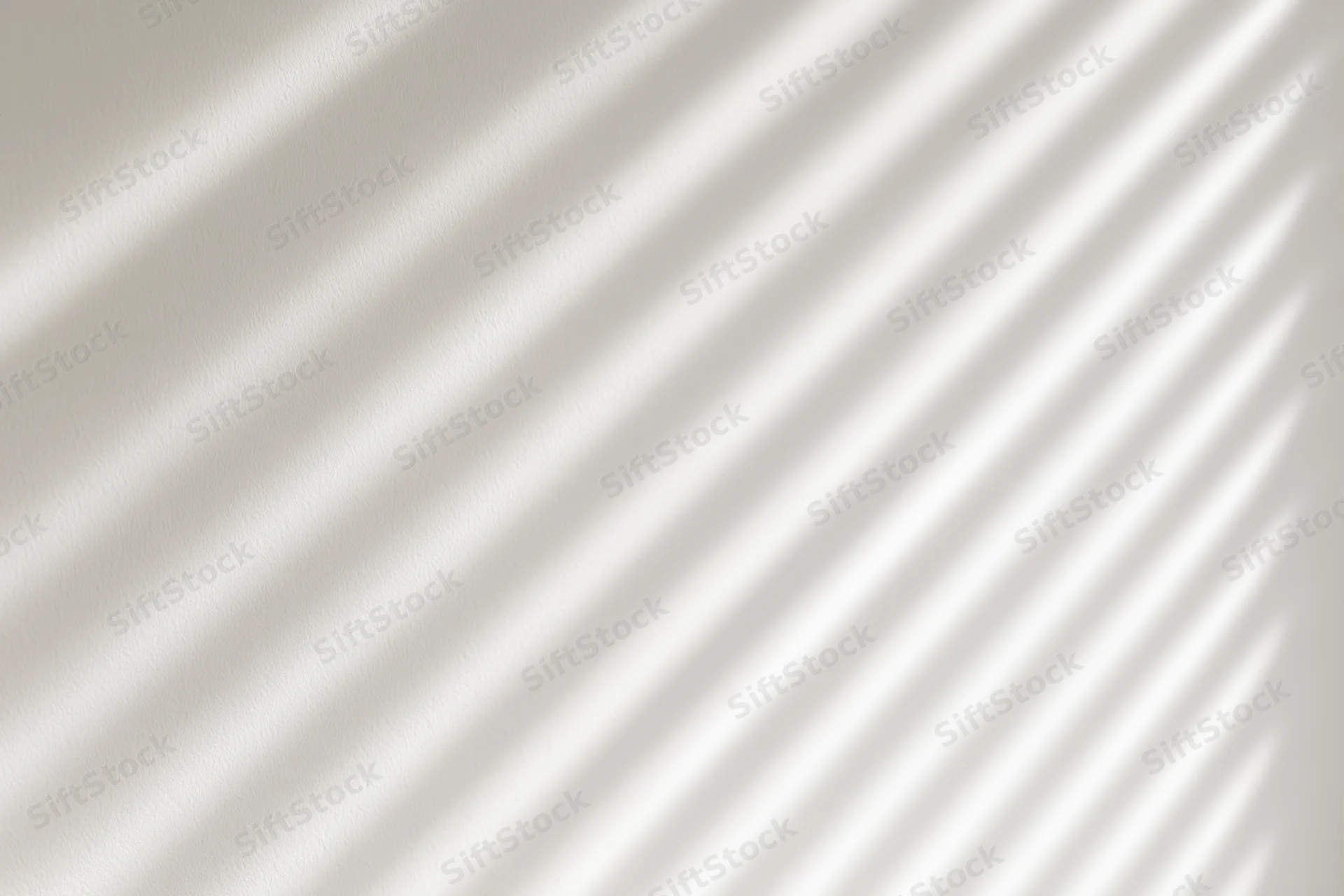 Diagonal shadows from window blinds cast across a plain white interior wall