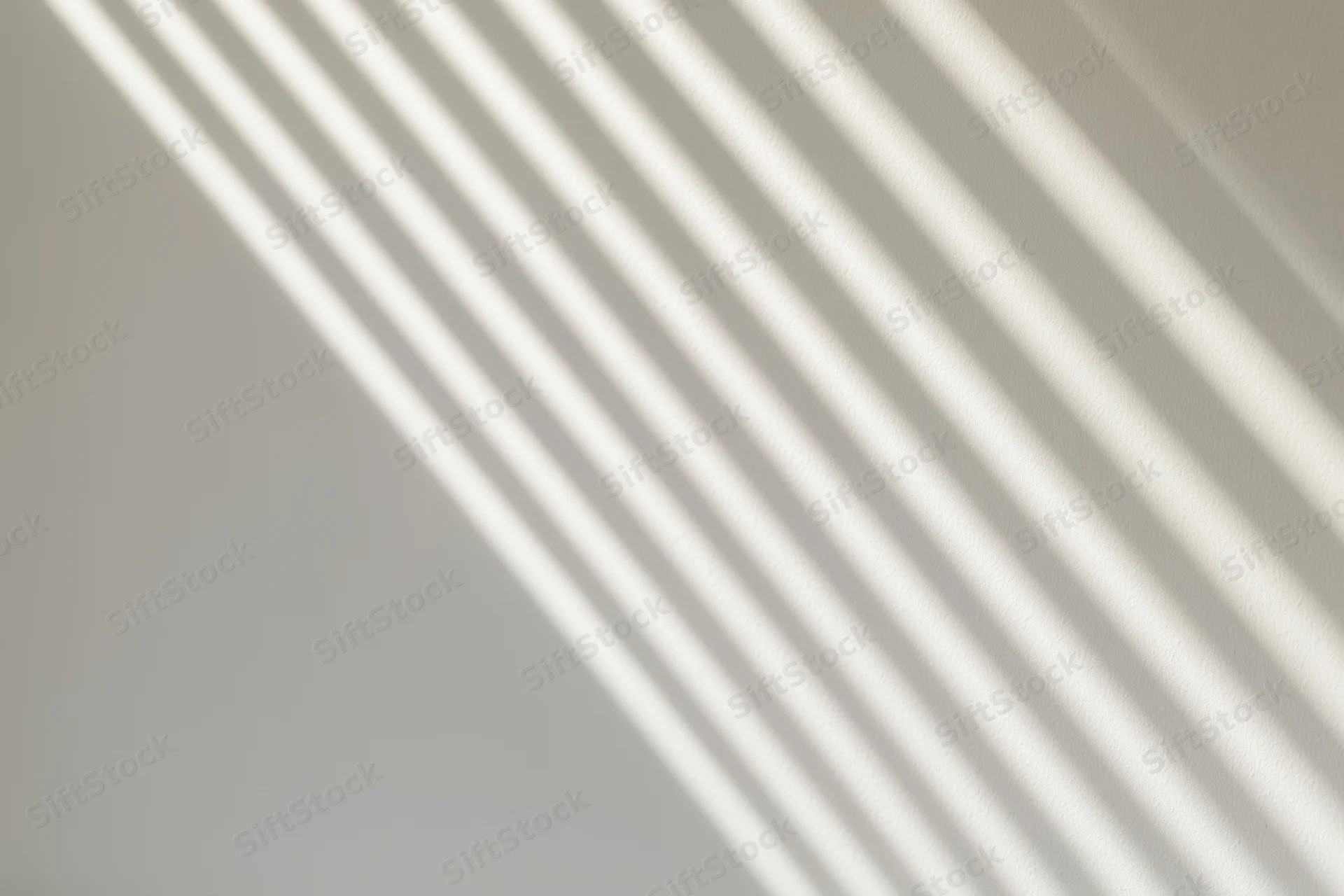 Diagonal shadows from window blinds cast across a plain white interior wall