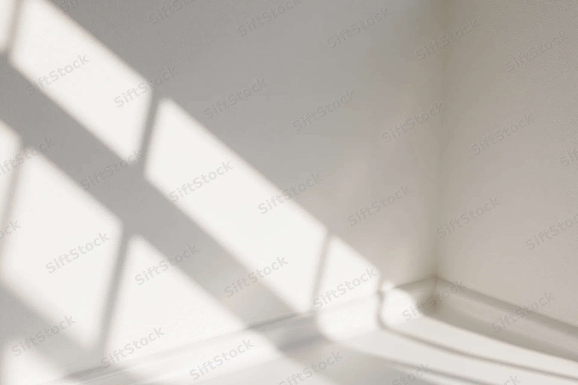 Diagonal shadows from a window frame cast across a white interior corner