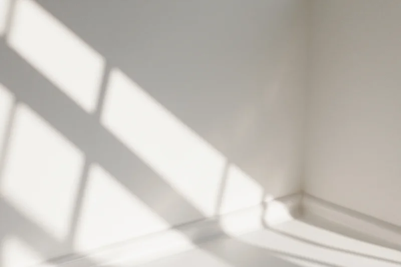 Diagonal shadows from a window frame cast across a white interior corner