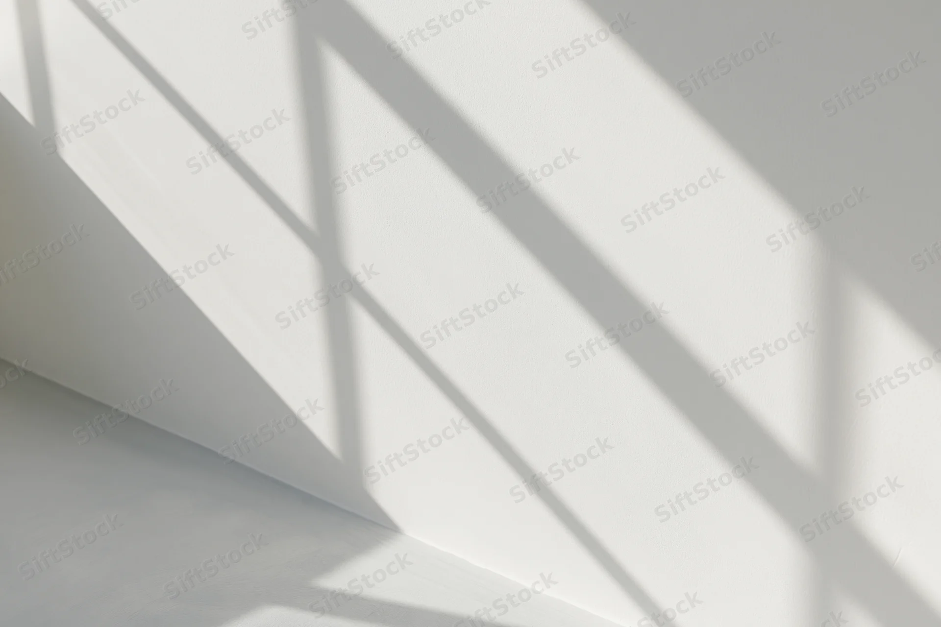 Diagonal shadows from window frames cast across a white interior wall and ceiling