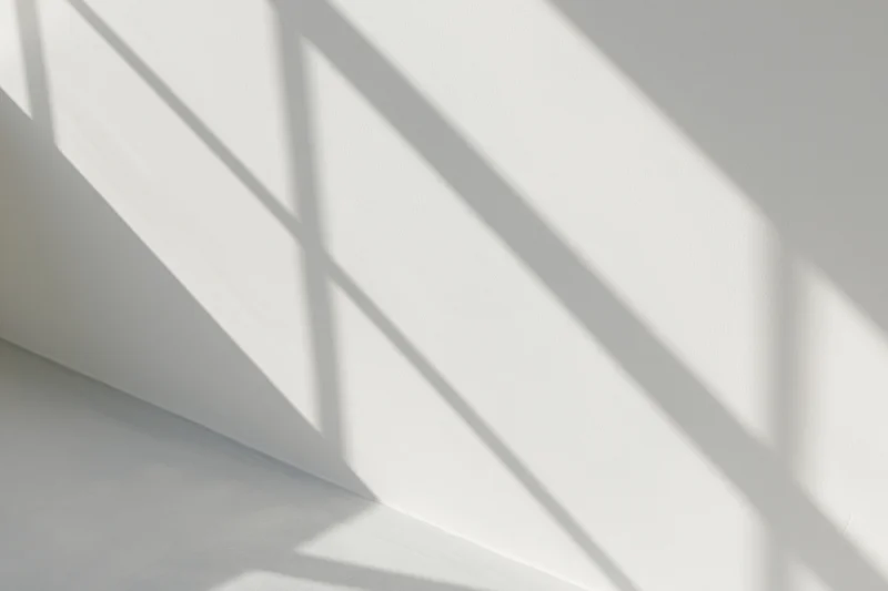Diagonal shadows from window frames cast across a white interior wall and ceiling