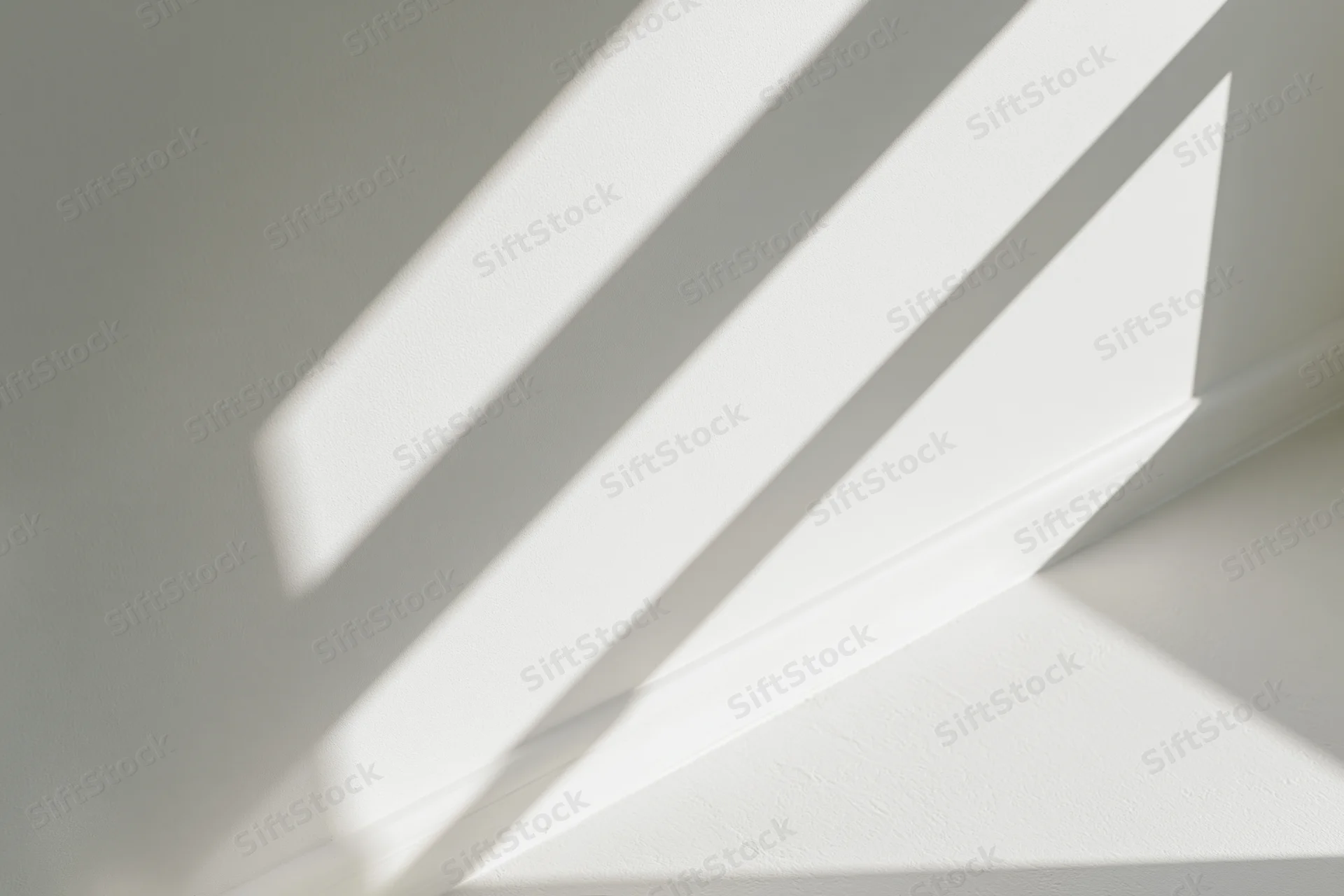 Diagonal shadows from a window frame cast across a white interior wall and ceiling