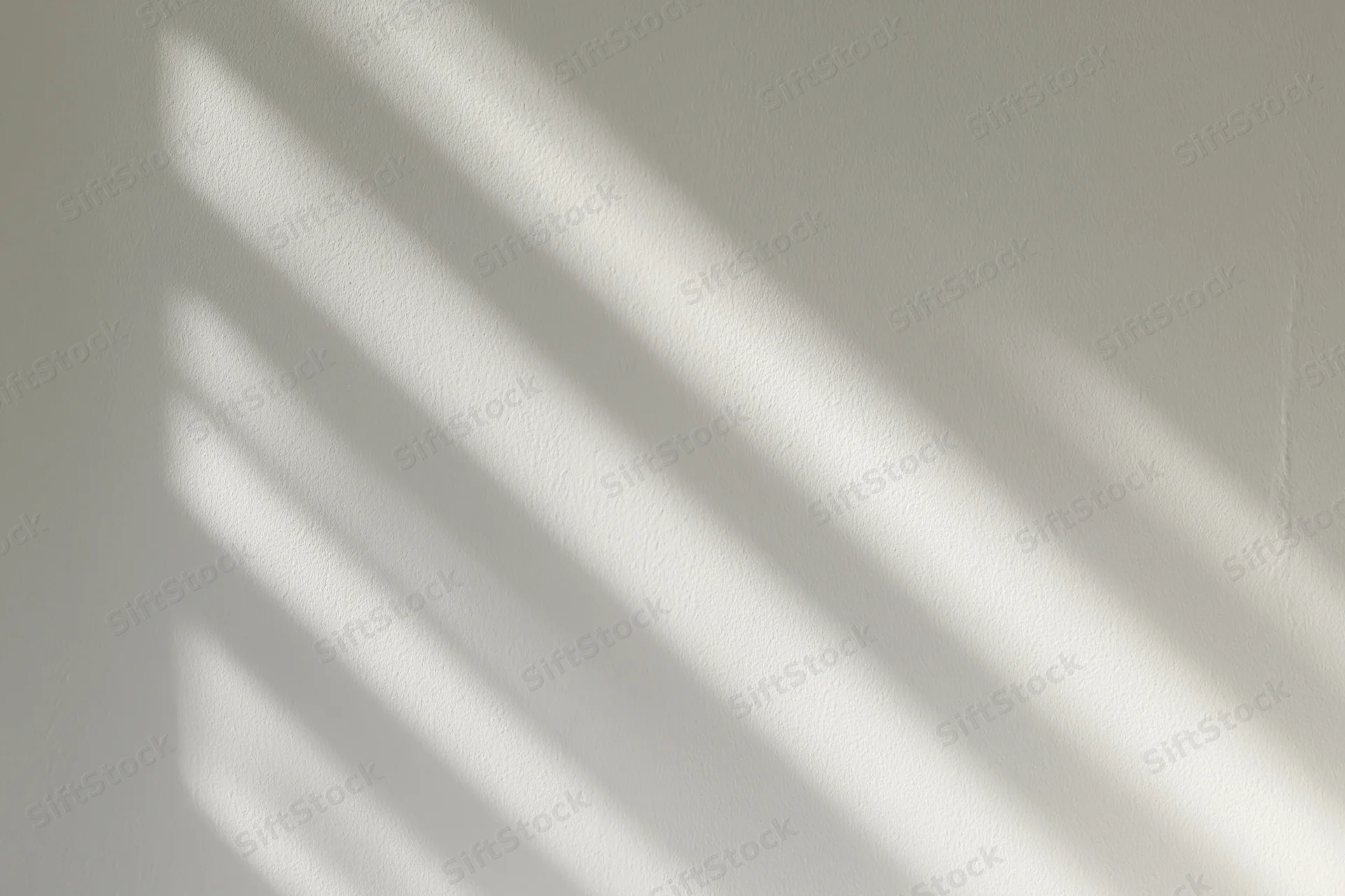 Diagonal bands of sunlight and shadow cast across a white interior wall