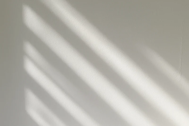 Diagonal bands of sunlight and shadow cast across a white interior wall