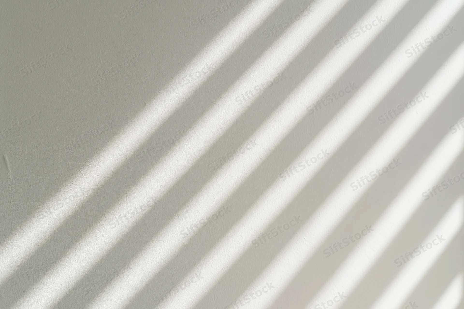 Diagonal light and shadow stripes from window blinds on a flat wall interior