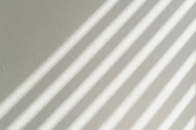 Diagonal light and shadow stripes from window blinds on a flat wall interior