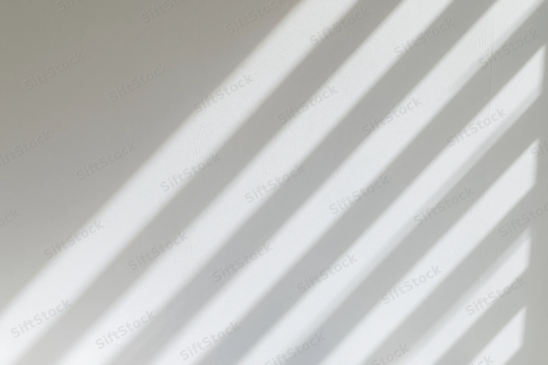 Diagonal bands of light and shadow from a window falling across a white wall indoors