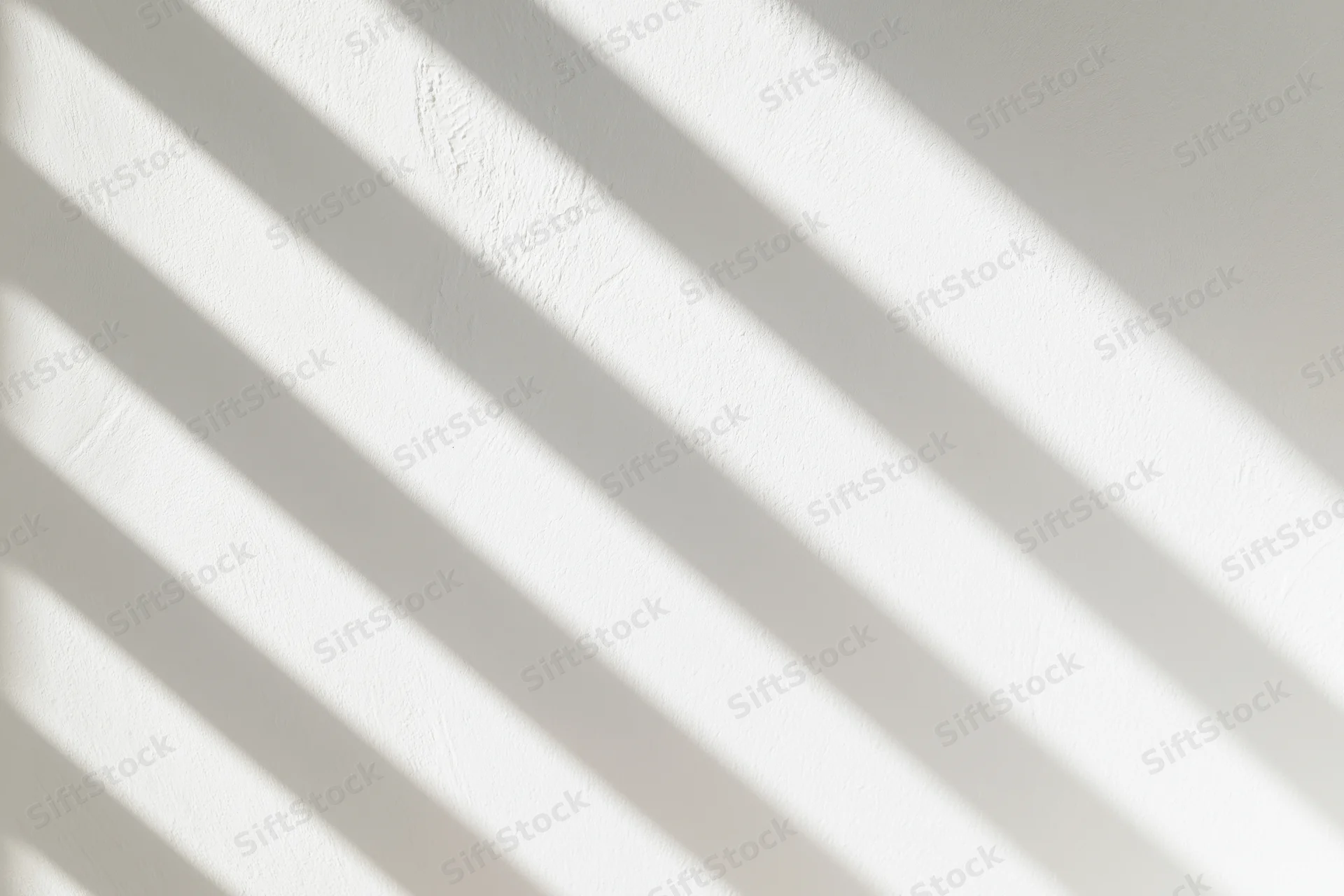 Diagonal bands of light and shadow cast across a white textured wall