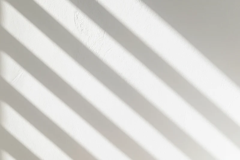Diagonal bands of light and shadow cast across a white textured wall