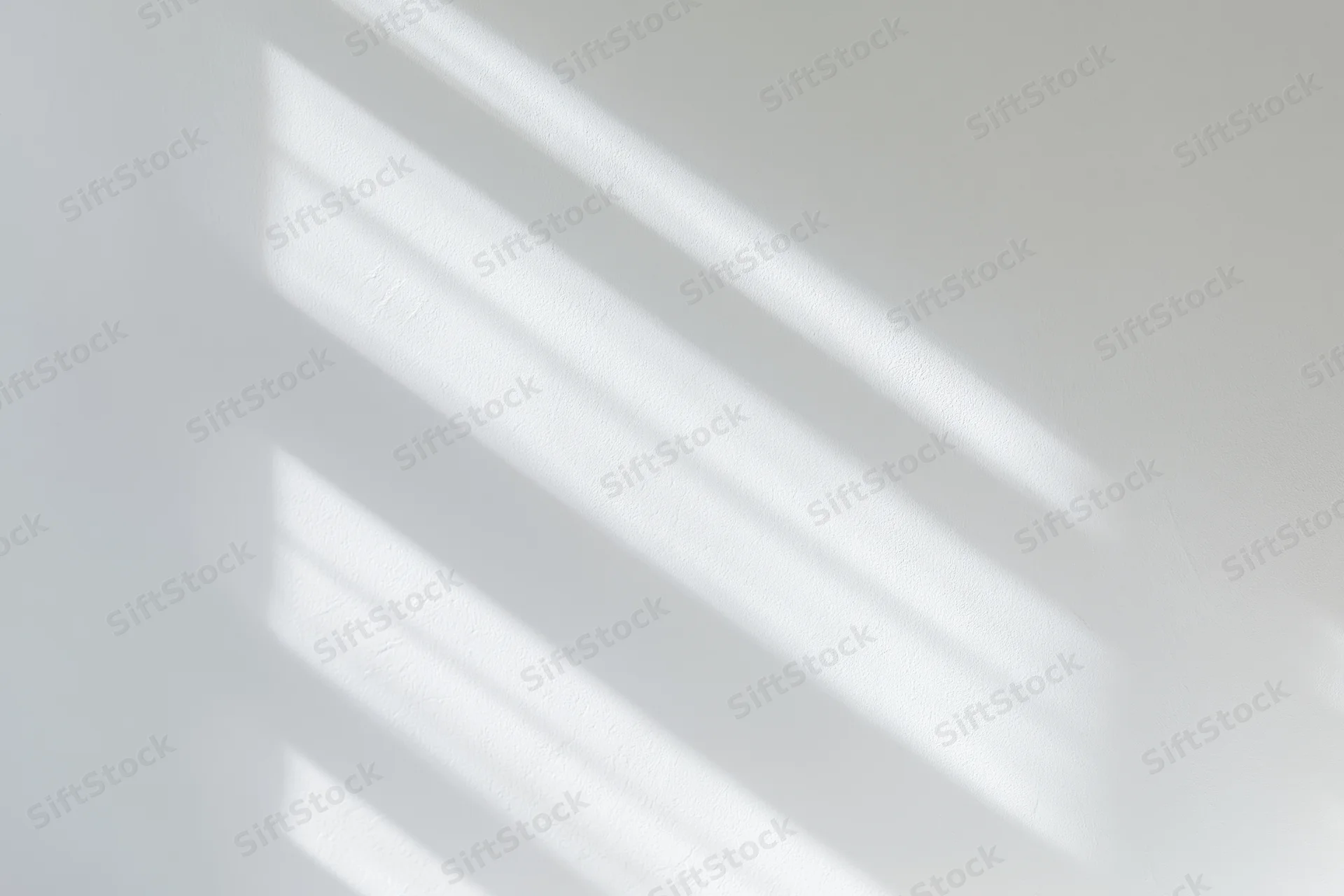 Diagonal light and shadow stripes cast across a white wall in an interior space