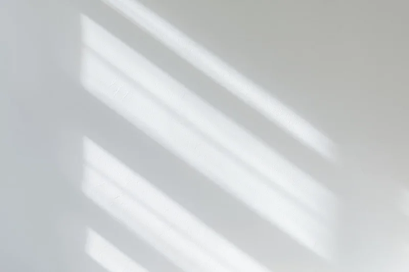 Diagonal light and shadow stripes cast across a white wall in an interior space