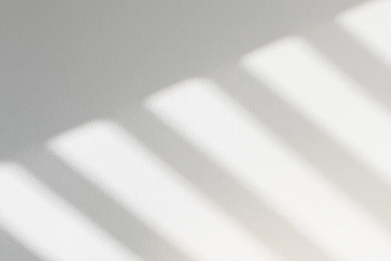 Diagonal light and shadow stripes cast across a plain wall surface