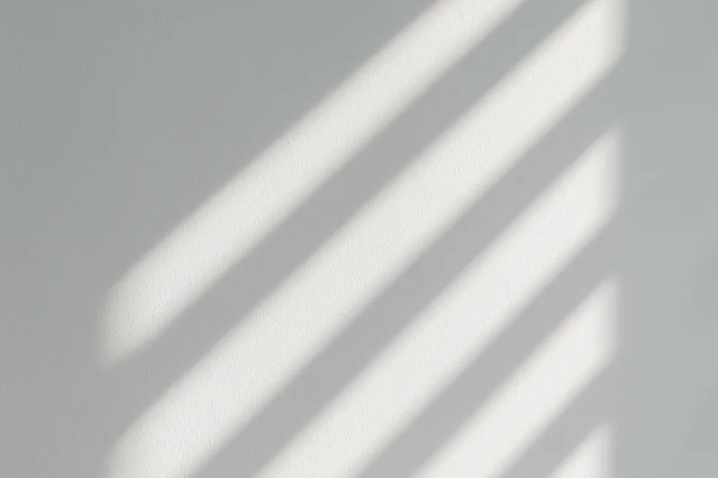 Diagonal light and shadow stripes cast across a plain wall indoors