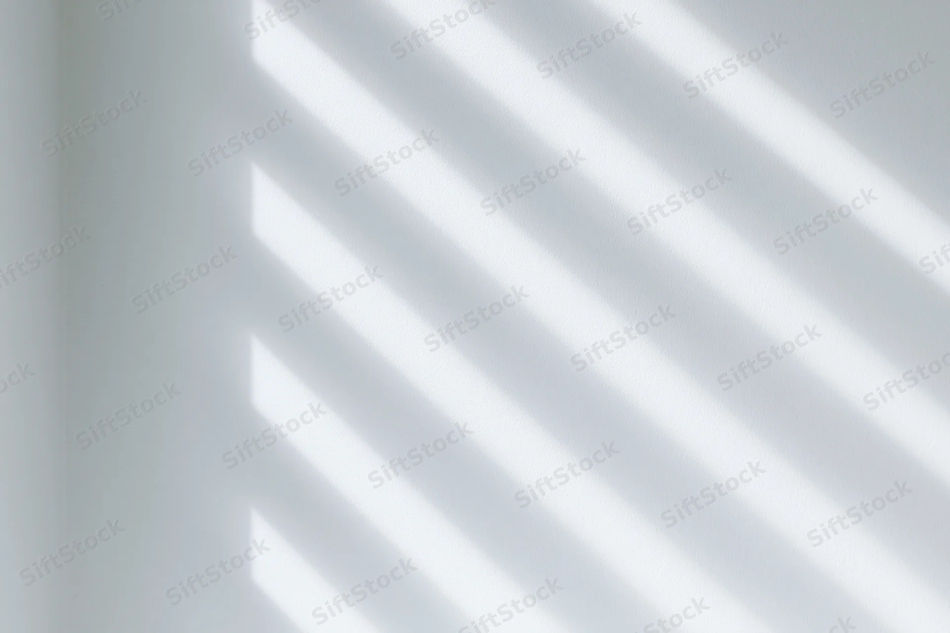 Diagonal light and shadow stripes cast across a plain white wall indoors