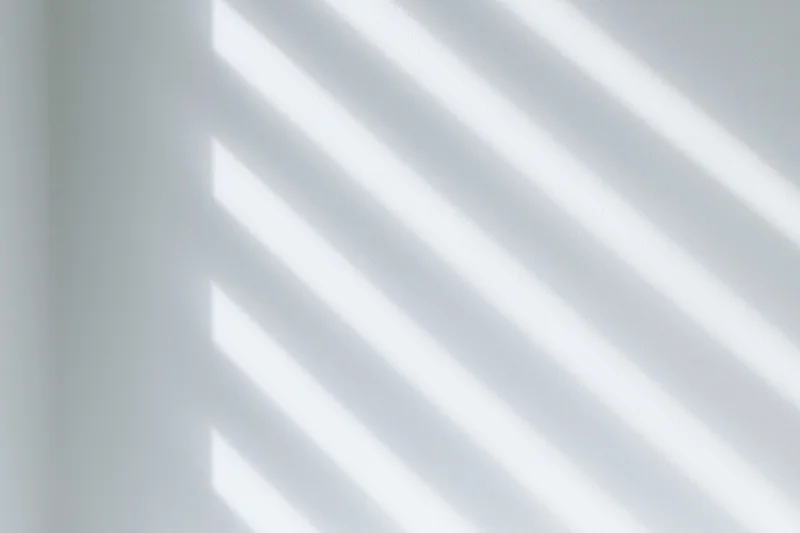 Diagonal light and shadow stripes cast across a plain white wall indoors