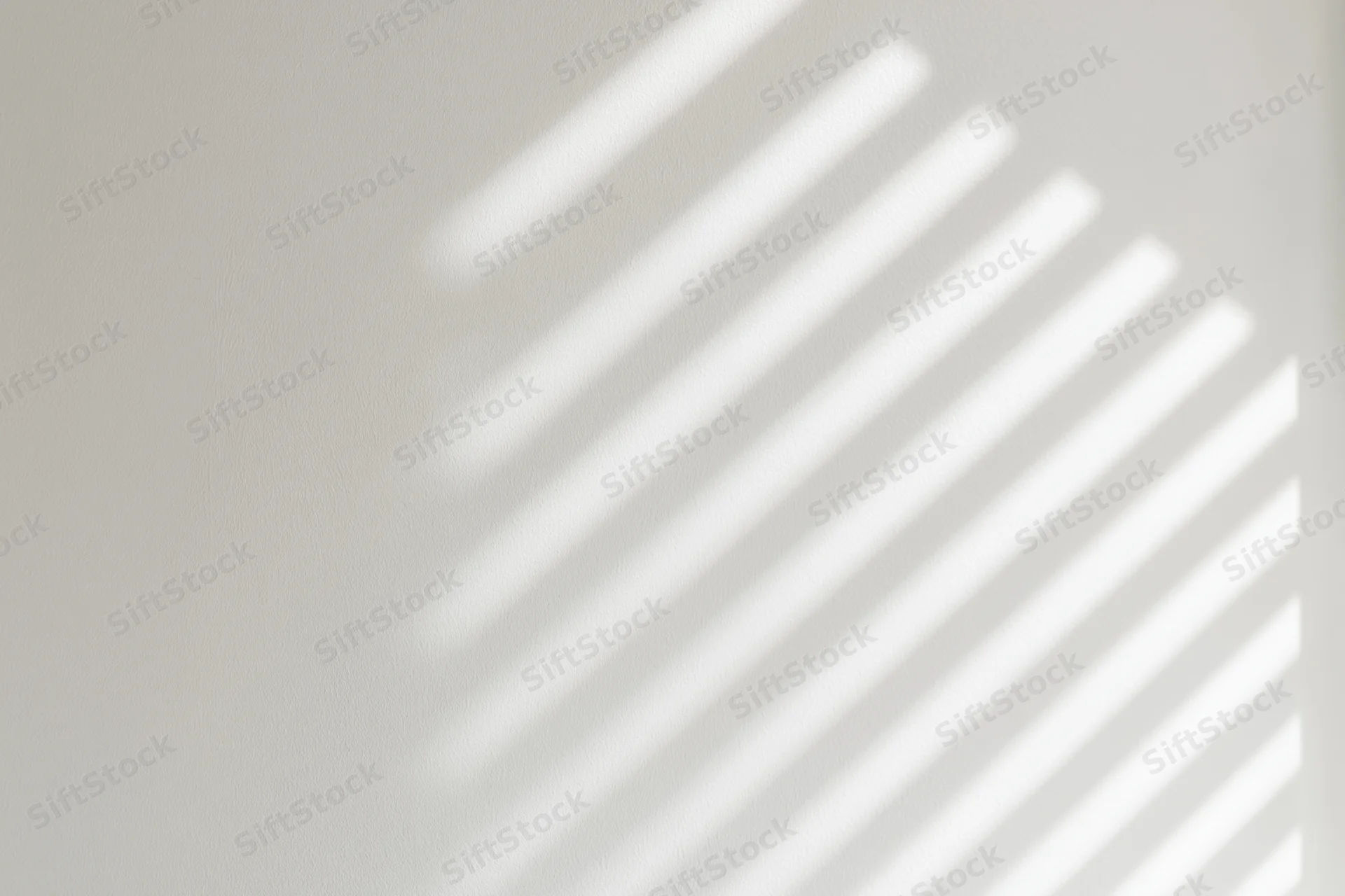 Diagonal light and shadow stripes from window blinds on a white wall