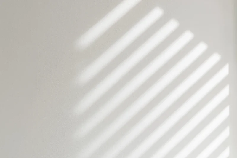 Diagonal light and shadow stripes from window blinds on a white wall