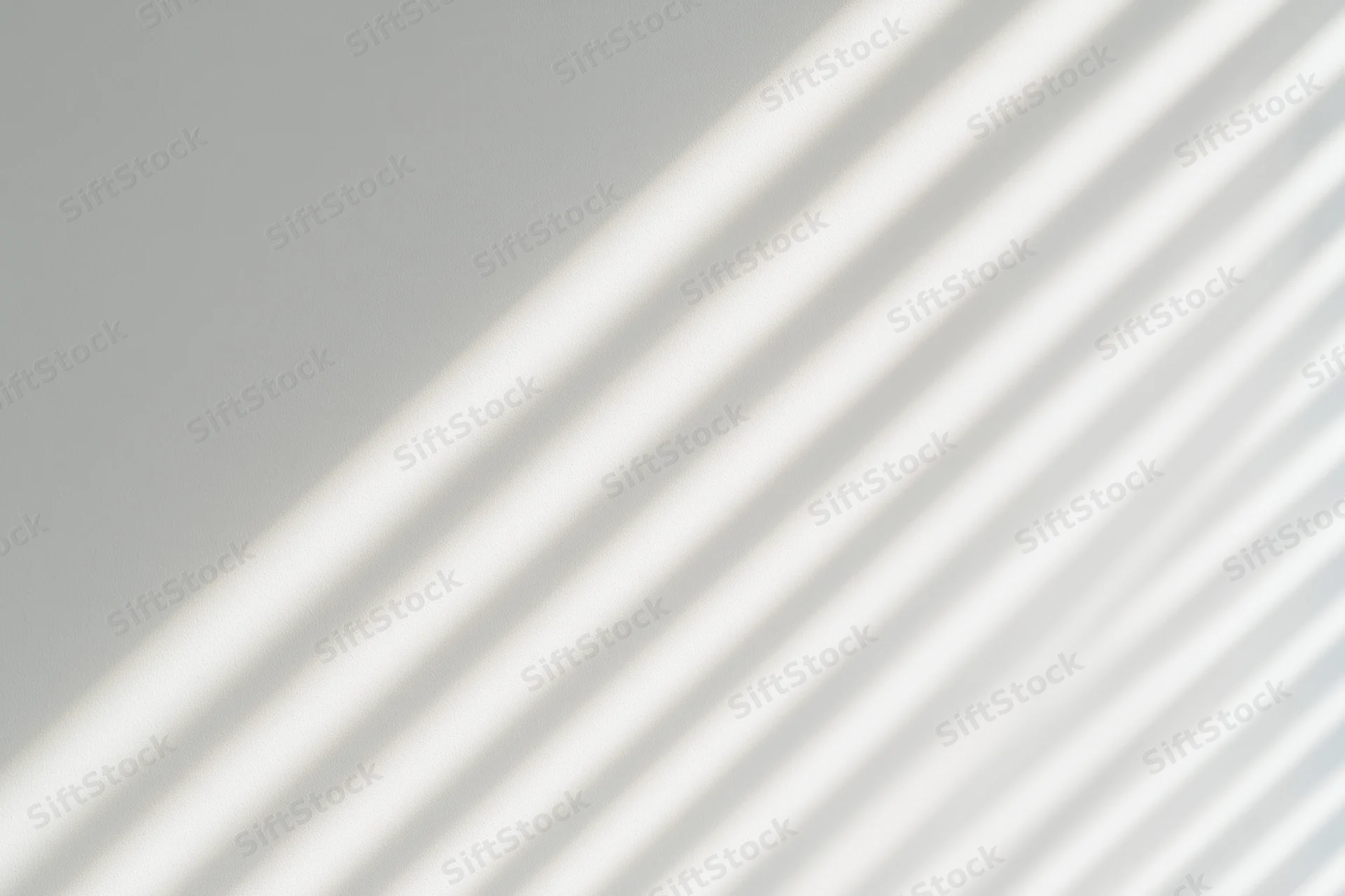Diagonal light and shadow stripes from window blinds on a plain wall
