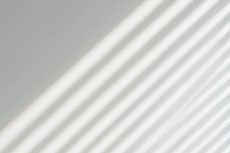 Diagonal light and shadow stripes from window blinds on a plain wall
